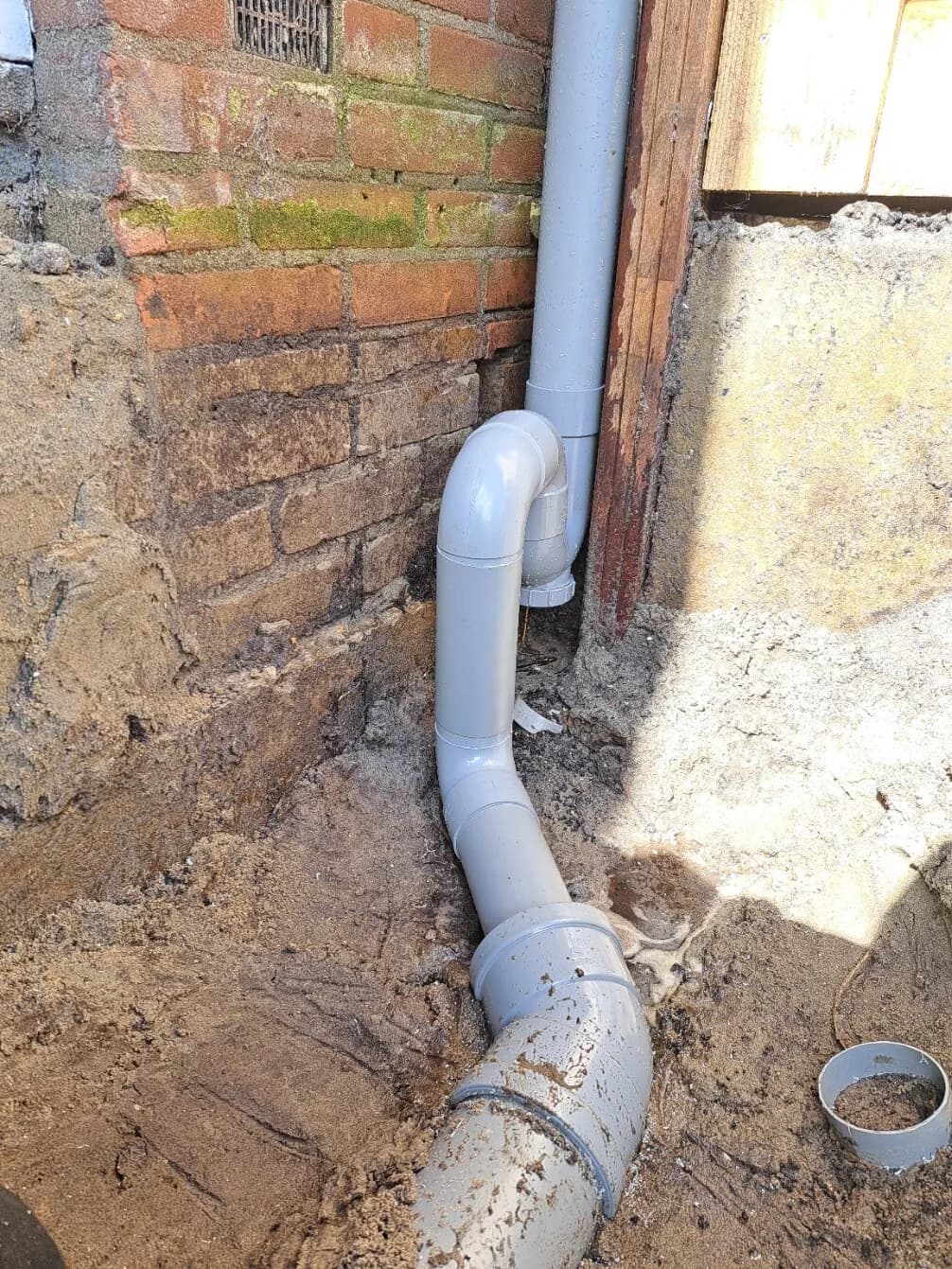 Nieuwe PVC-hemelwatersifon naast de gevel.