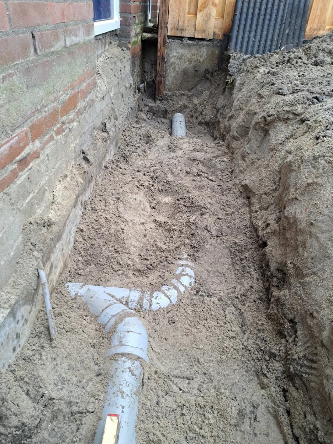 Nieuwe PVC-leiding met vertakking aangelegd in een uitgegraven tuin.